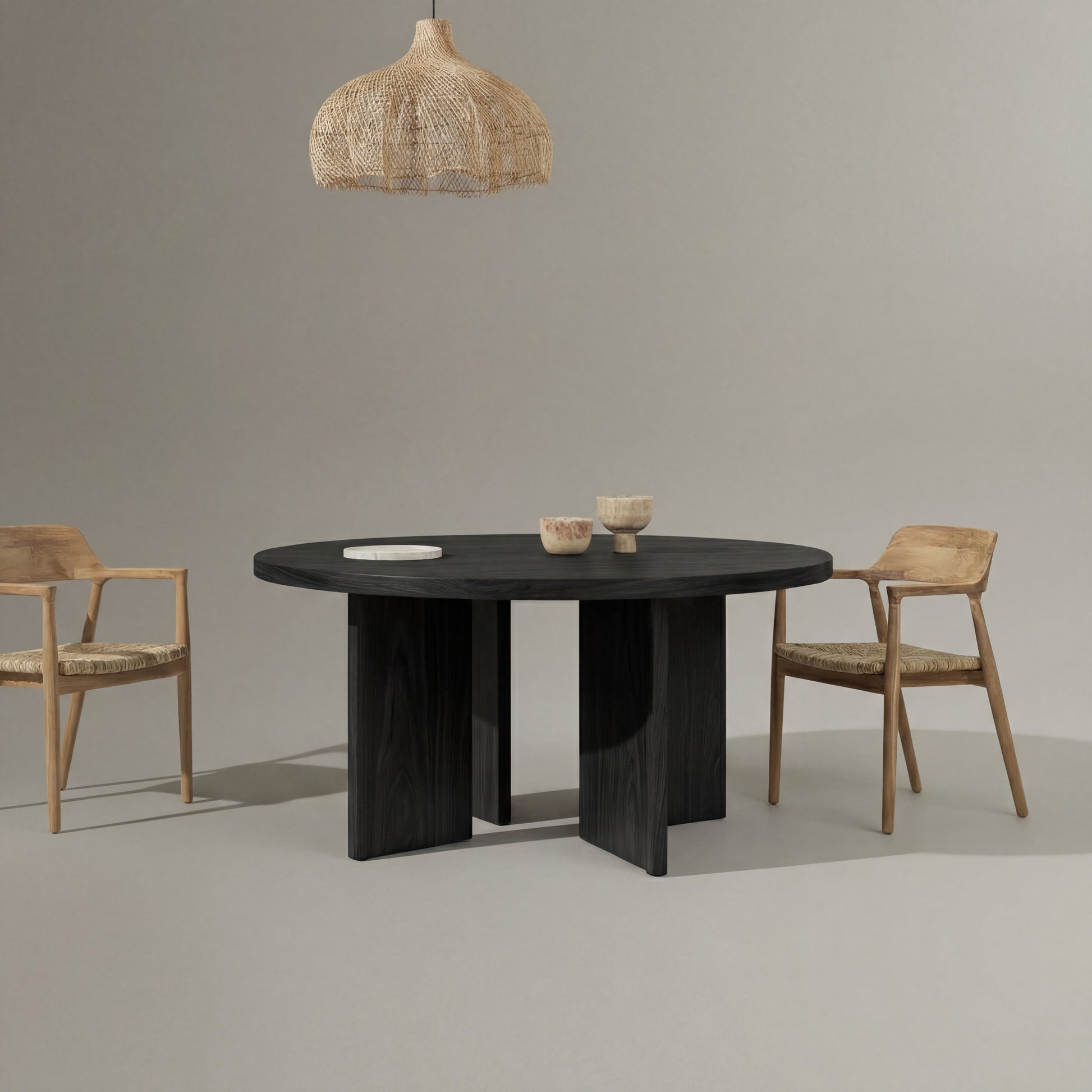 Black round table with two wooden chairs and a woven pendant light against a gray background